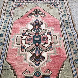 May include: A vintage pink and green rug with a traditional floral pattern. The rug has a fringed edge and is made of wool.