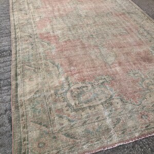 May include: A vintage rug with a faded pink and green floral pattern. The rug has a distressed look and is made of a soft, woven material.
