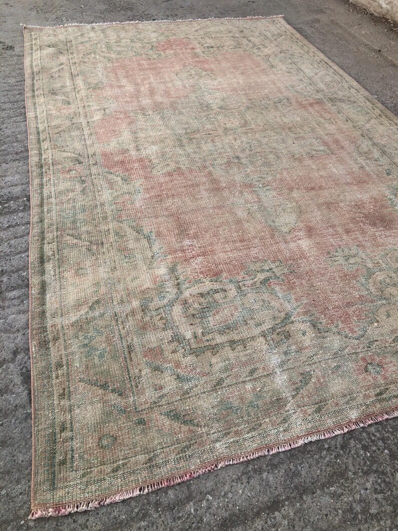 May include: A vintage rug with a faded pink and green floral pattern. The rug has a distressed look and is made of a soft, woven material.