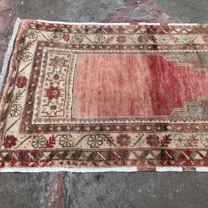 May include: A vintage runner rug with a faded pink center and intricate floral and geometric patterns in shades of brown, beige, and cream. The rug has a white fringe border.