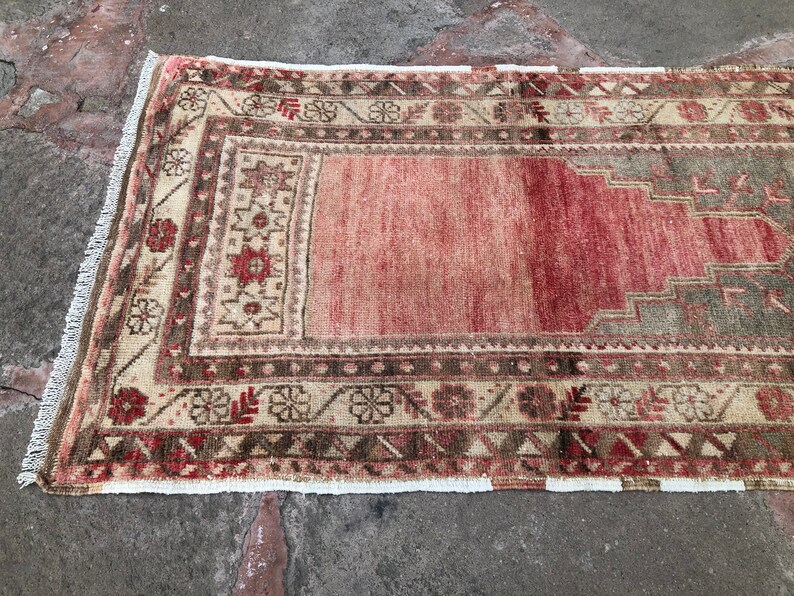 May include: A vintage runner rug with a faded pink center and intricate floral and geometric patterns in shades of brown, beige, and cream. The rug has a white fringe border.