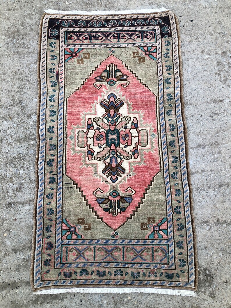 May include: A vintage rug with a pink, green, and blue geometric pattern. The rug has a fringe border and is made of wool.
