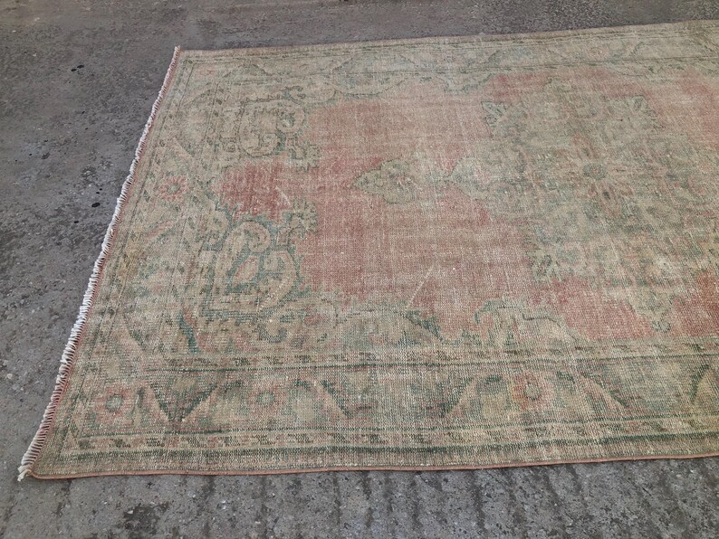 May include: A vintage rug with a faded pink and green floral pattern. The rug has a distressed look and is made of a soft, woven material.