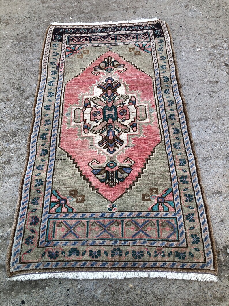 May include: A vintage Turkish rug with a pink and green geometric pattern. The rug has a fringed edge and is made of wool.