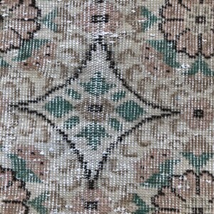 May include: A vintage rug with a diamond pattern in the center and floral designs on the sides. The rug is beige with green and brown accents.