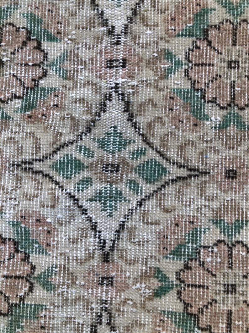May include: A vintage rug with a diamond pattern in the center and floral designs on the sides. The rug is beige with green and brown accents.