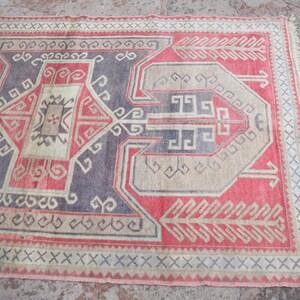 May include: A vintage Turkish rug with a geometric pattern in shades of red, beige, and blue. The rug has a fringe border and is woven with a traditional design.