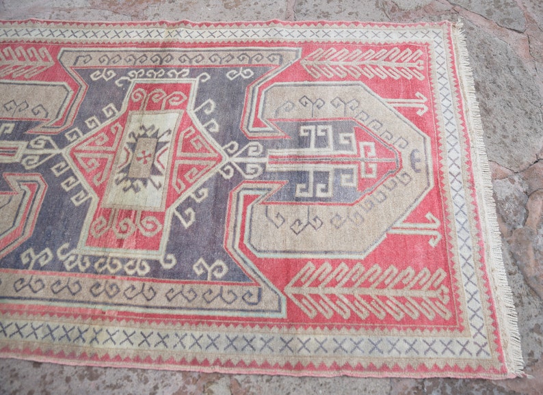 May include: A vintage Turkish rug with a geometric pattern in shades of red, beige, and blue. The rug has a fringe border and is woven with a traditional design.