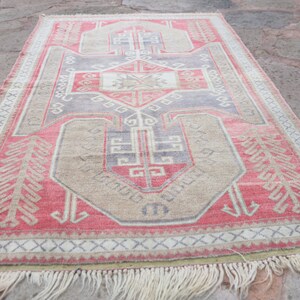 May include: A vintage Turkish rug with a geometric pattern in shades of red, beige, and gray. The rug has a fringe border and is made of wool.