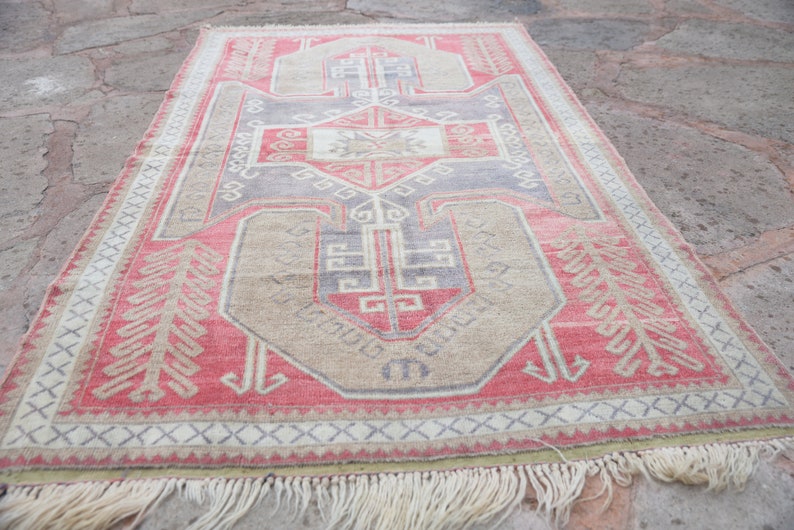 May include: A vintage Turkish rug with a geometric pattern in shades of red, beige, and gray. The rug has a fringe border and is made of wool.