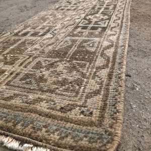 Puede incluir: Una alfombra larga y estrecha con un patrón geométrico en tonos marrones, beige y grises. La alfombra tiene flecos en ambos extremos.