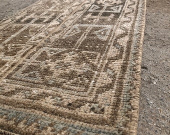 May include: A long, narrow rug with a geometric pattern in shades of brown, beige, and gray. The rug has a fringe on both ends.