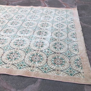 May include: A vintage rug with a repeating pattern of green, white, and pink floral motifs. The rug has a light beige background and a pink border.