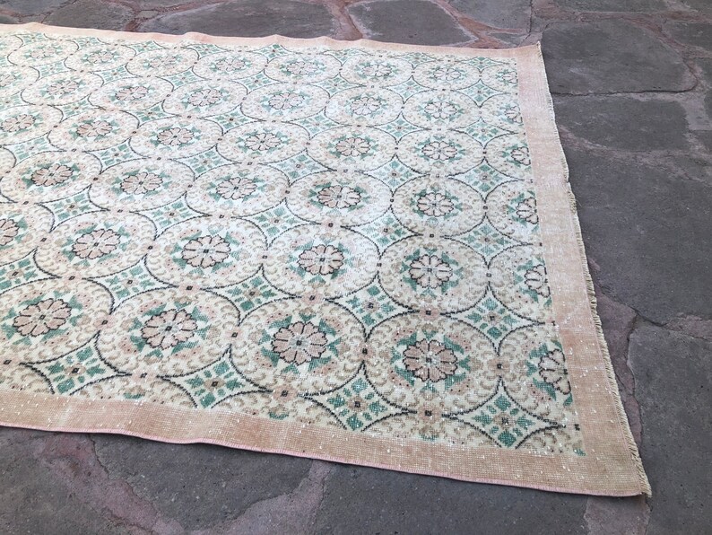 May include: A vintage rug with a repeating pattern of green, white, and pink floral motifs. The rug has a light beige background and a pink border.
