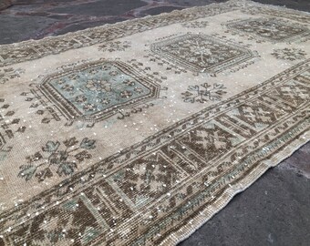 May include: A vintage off-white rug with a faded brown and blue geometric pattern. The rug has a distressed look and is perfect for adding a touch of bohemian style to any room.