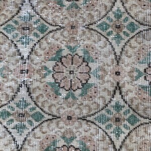 May include: A close-up of a beige and green patterned rug with a floral design. The rug has a distressed look and is made of a woven material.