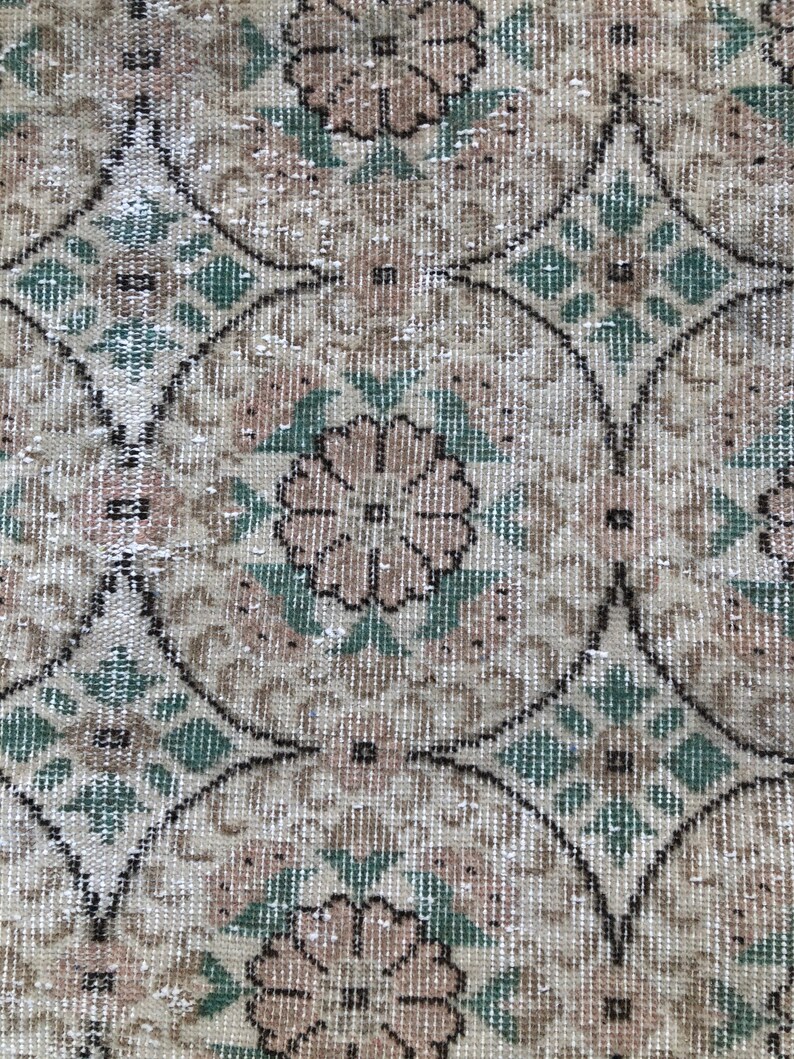 May include: A close-up of a beige and green patterned rug with a floral design. The rug has a distressed look and is made of a woven material.