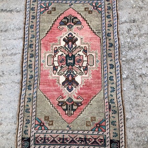May include: A vintage Turkish rug with a pink and green geometric pattern. The rug has a fringe border and is in good condition.