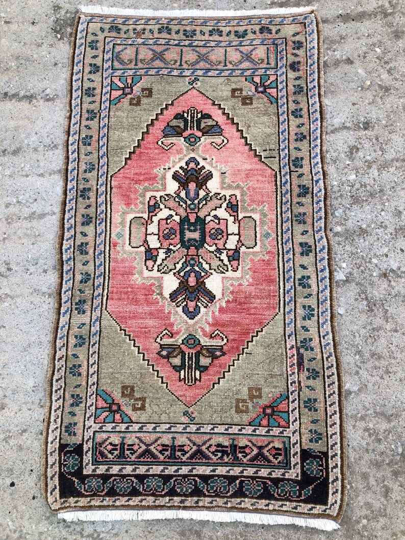 May include: A vintage Turkish rug with a pink and green geometric pattern. The rug has a fringe border and is in good condition.