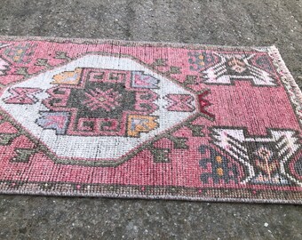 May include: A pink and white runner rug with a geometric pattern. The rug has a fringe border and is made of woven fabric.
