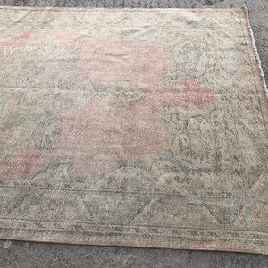 May include: A vintage rug with a faded pink and green floral pattern. The rug has a distressed look and is made of a soft, woven material.