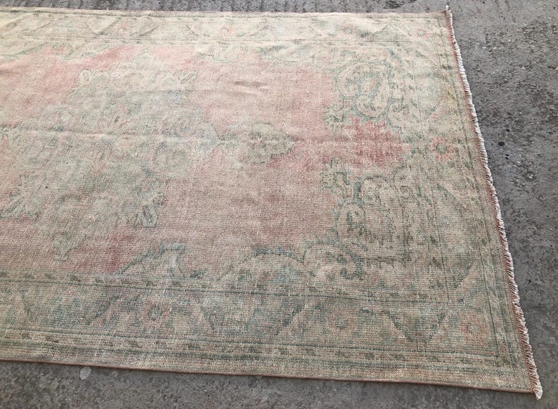 May include: A vintage rug with a faded pink and green floral pattern. The rug has a distressed look and is made of a soft, woven material.