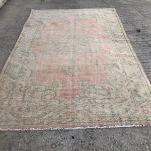 May include: A vintage rug with a faded pink and green floral pattern. The rug has a distressed look and a fringed edge.
