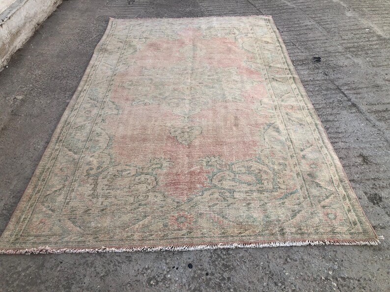 May include: A vintage rug with a faded pink and green floral pattern. The rug has a distressed look and a fringed edge.