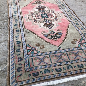 May include: A vintage Turkish runner rug with a pink and green floral pattern. The rug has a fringe border and is made of wool.