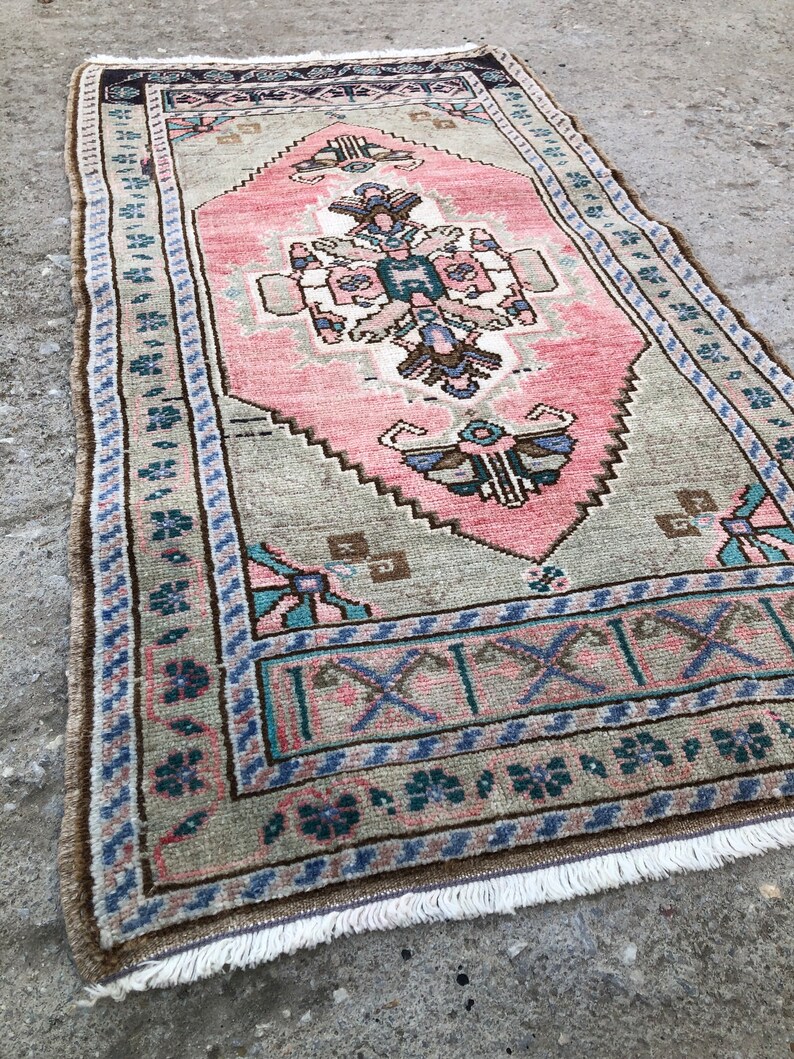 May include: A vintage Turkish runner rug with a pink and green floral pattern. The rug has a fringe border and is made of wool.