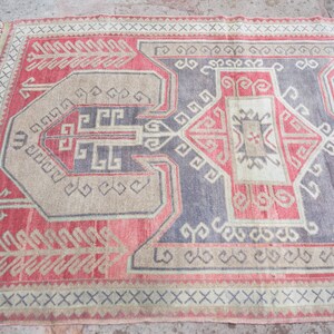 May include: A vintage rug with a geometric pattern in shades of red, beige, and gray. The rug has a fringe border and is woven with intricate details.