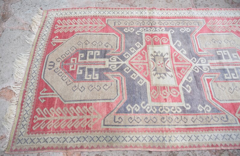 May include: A vintage rug with a geometric pattern in shades of red, beige, and gray. The rug has a fringe border and is woven with intricate details.