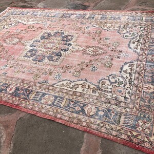 May include: A vintage pink and cream rug with a floral pattern and a blue border. The rug has a distressed look and is perfect for adding a touch of bohemian style to your home.