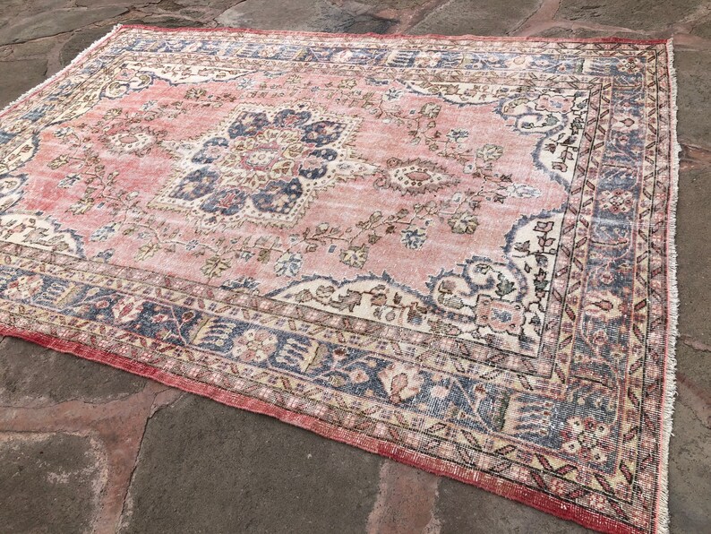 May include: A vintage pink and cream rug with a floral pattern and a blue border. The rug has a distressed look and is perfect for adding a touch of bohemian style to your home.