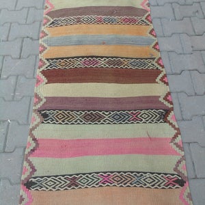 May include: A long, narrow, multi-colored rug with a striped pattern. The rug is made of woven wool and features a variety of colors, including brown, pink, beige, and blue.