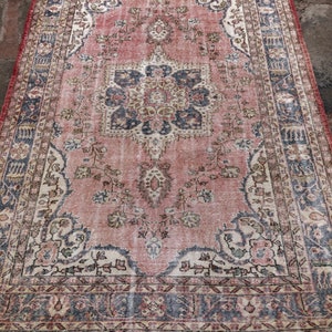 May include: A vintage pink and cream rug with a floral pattern and a central medallion. The rug has a faded, distressed look and a fringed edge.