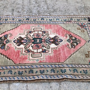 May include: A vintage rug with a pink and green color scheme. The rug has a central medallion with a floral design and a border with a geometric pattern.