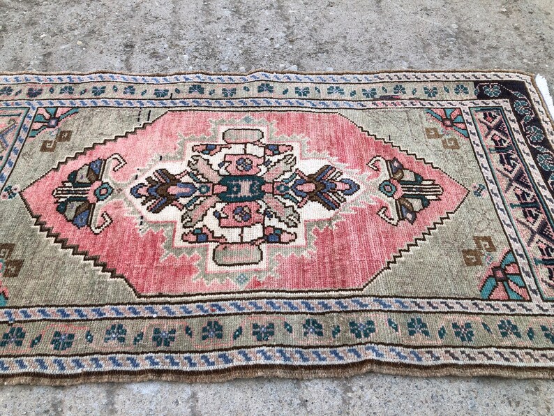 May include: A vintage rug with a pink and green color scheme. The rug has a central medallion with a floral design and a border with a geometric pattern.