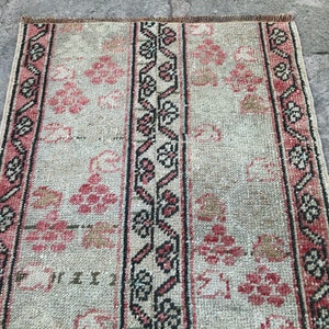May include: A rectangular rug with a faded, vintage appearance. The rug features a central design of alternating vertical stripes. The stripes include floral patterns in shades of pink and beige, bordered by black and pink decorative elements.