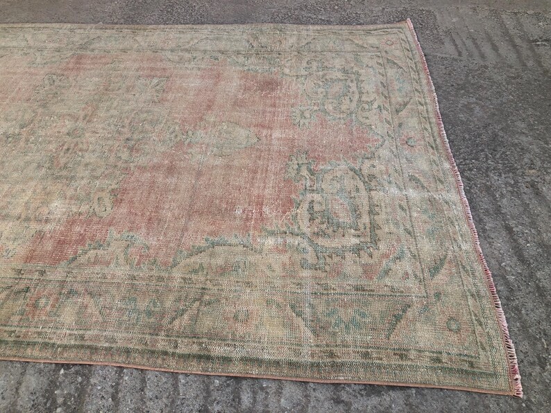 May include: A vintage rug with a faded pink and green floral pattern. The rug has a distressed look and is made of a soft, woven material.