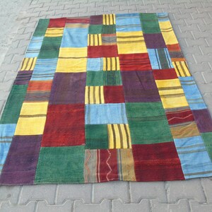 May include: A rectangular patchwork rug with a vibrant mix of colors. The rug features squares of red, yellow, blue, green, and purple, with some squares having striped patterns. The rug is laid out on a gray surface.