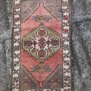 Könnte beinhalten: Ein antiker türkischer Teppich mit einem floralen Muster und einem Fransenrand. Die dominierenden Farben sind Rosa, Grün und Braun.