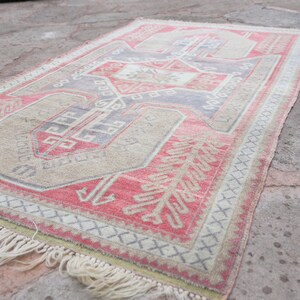 May include: A vintage Turkish rug with a red, beige, and blue geometric pattern. The rug has a fringe border and is lying on a concrete surface.