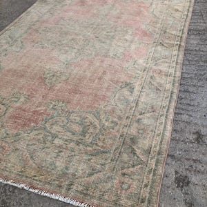 May include: A vintage rug with a faded pink and green floral pattern. The rug has a fringed edge and is made of wool.