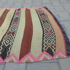 May include: A handwoven rug with a striped pattern in shades of brown, beige, and pink. The rug has a fringe border and intricate geometric designs.