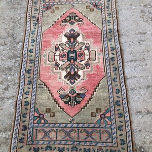 May include: A vintage Turkish rug with a pink and green geometric pattern. The rug has a fringe border and is in good condition.