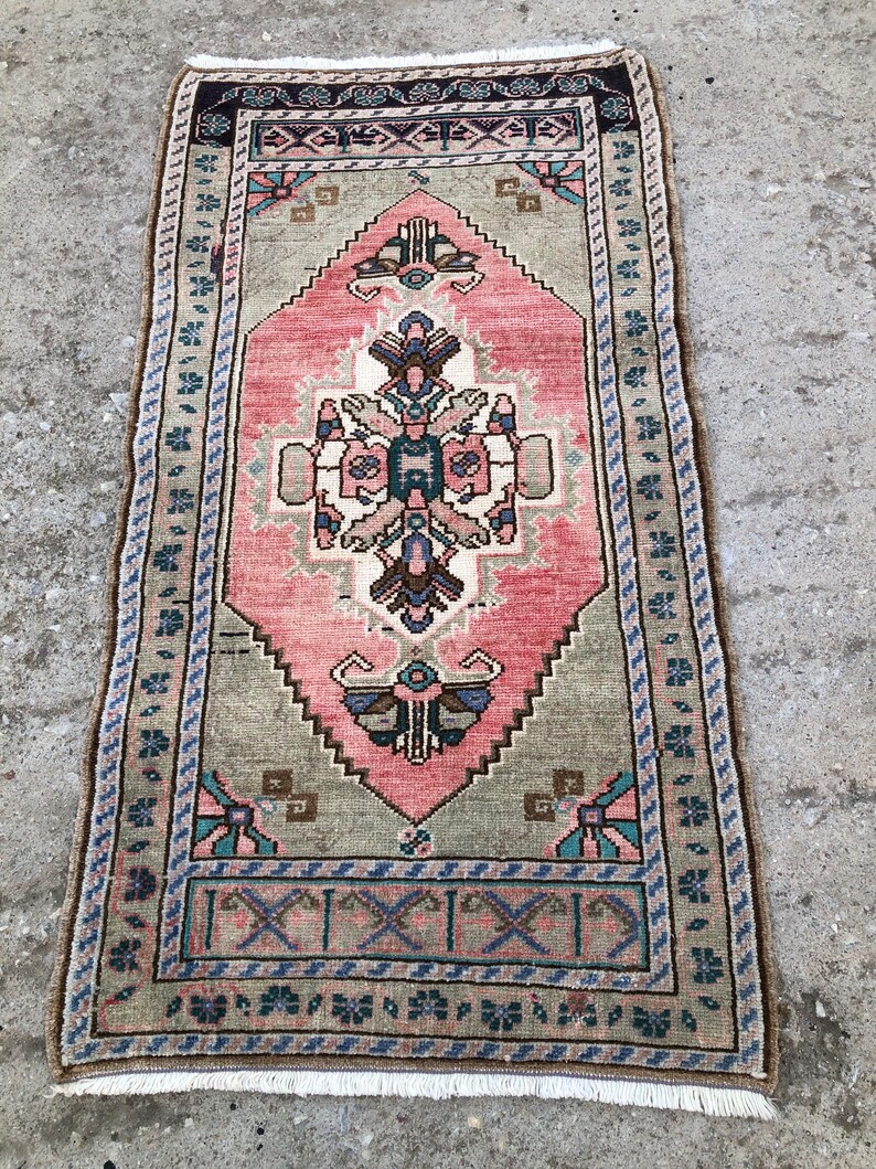 May include: A vintage Turkish rug with a pink and green geometric pattern. The rug has a fringe border and is in good condition.