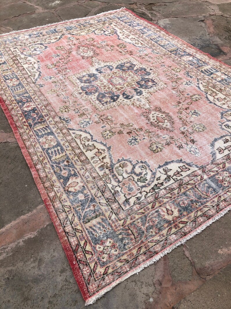 May include: A vintage pink and cream rug with a floral pattern and a blue and cream border. The rug has a fringed edge.