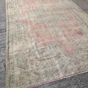 May include: A vintage rug with a faded pink and green floral pattern. The rug has a fringed edge and is made of a soft, woven material.
