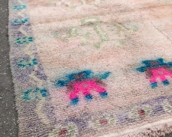 Peut inclure: Un tapis rose et blanc avec un motif géométrique bleu et rose. Le tapis a une bordure frangée.